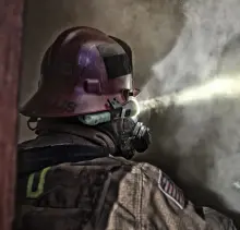 Firefighter using a high-visibility yellow flashlight by Pelican as they work in a smokey area.
